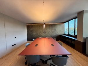 Sala riunioni, vista d’insieme: tavolo terracotta, parete decorativa, mobile lungo la finestra